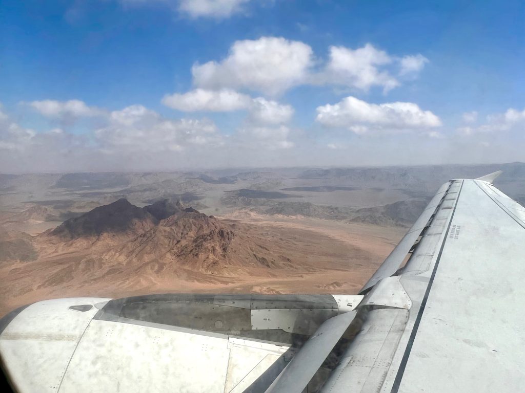 View out of a plane window showing part of the wing and a dry, raised brown landscape below