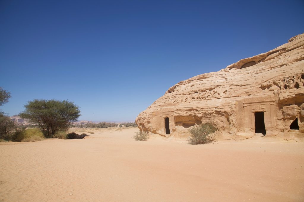 desert scape with several tombs carved into the rock cliffs 