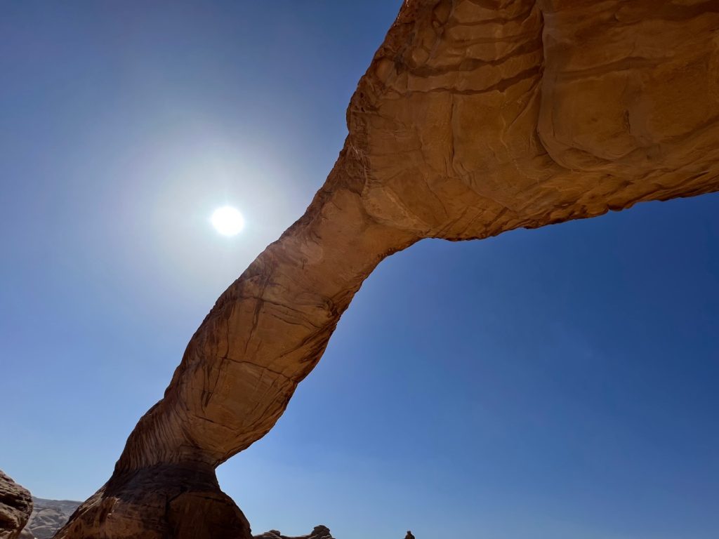 a large rock arch beneath blue sky and the sun