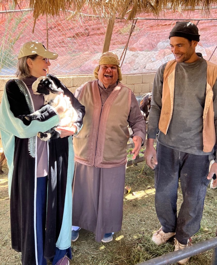 a woman holding a goats stands besides two men with all three people laughing