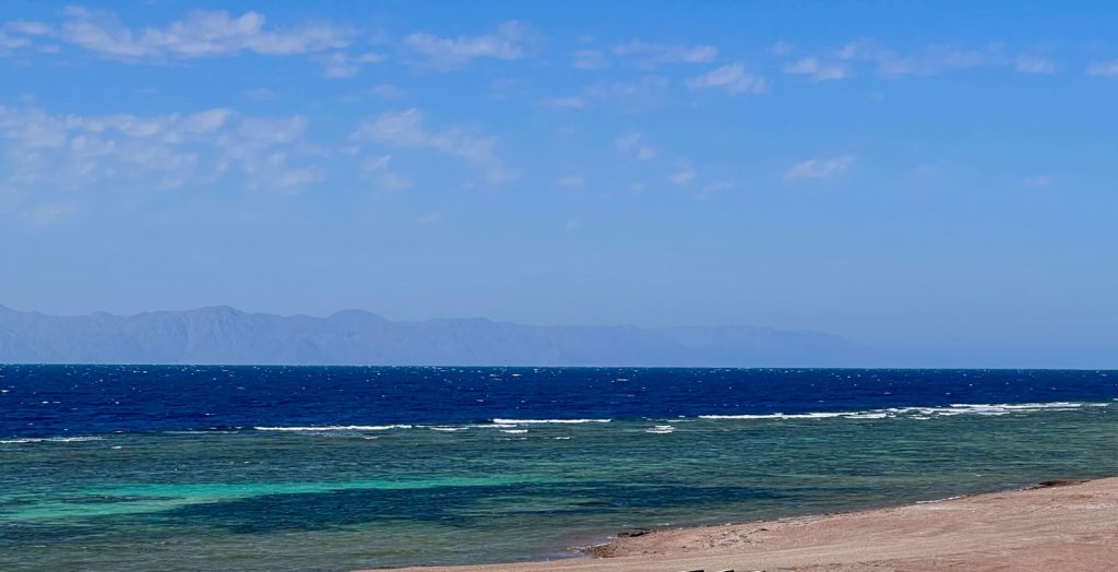 a beach with blue water and hills in the distance