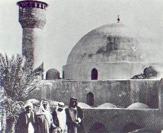 an old photo of several men in Arab dress in front of a mosque's dome and minerat