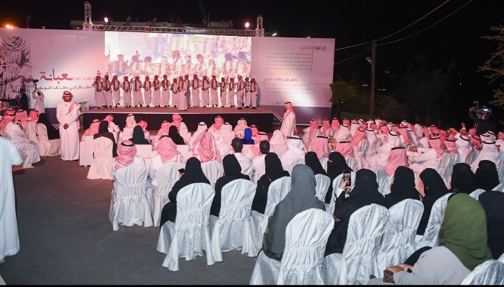 an audience of Saudi Arabian men and women seated watching a performance on a stage