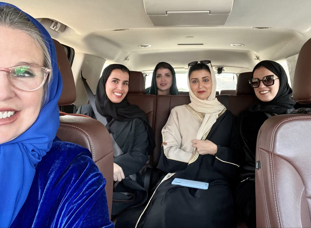 five women in black or blue abayas sit as passengers inside a luxury SUV