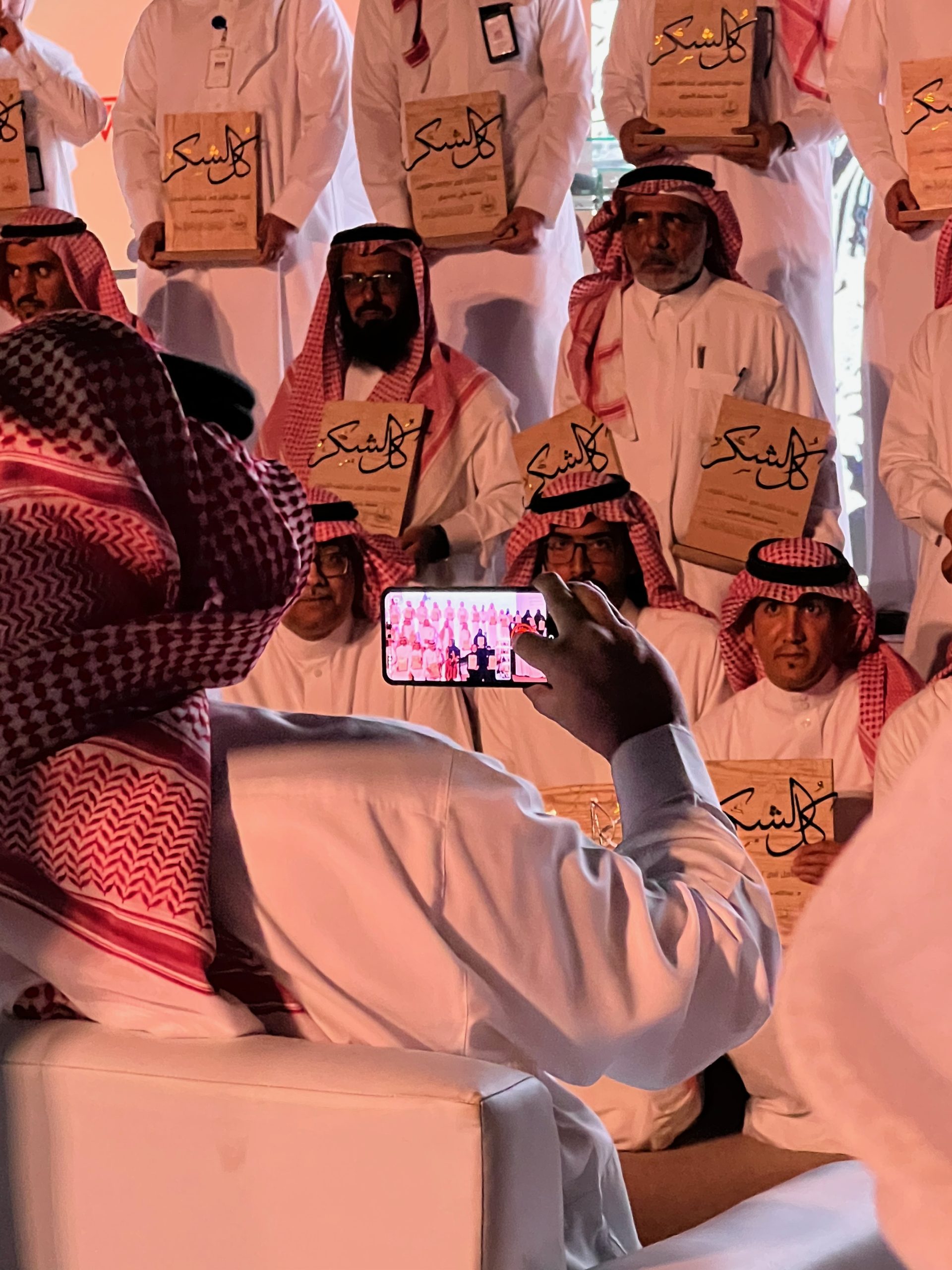 a photograph is taken of a group of men in white thobes as they hold commemorative plaques