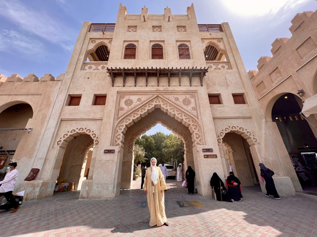 a woman in a colorful abaya stands in front of an ornamentally-decorated stone gate