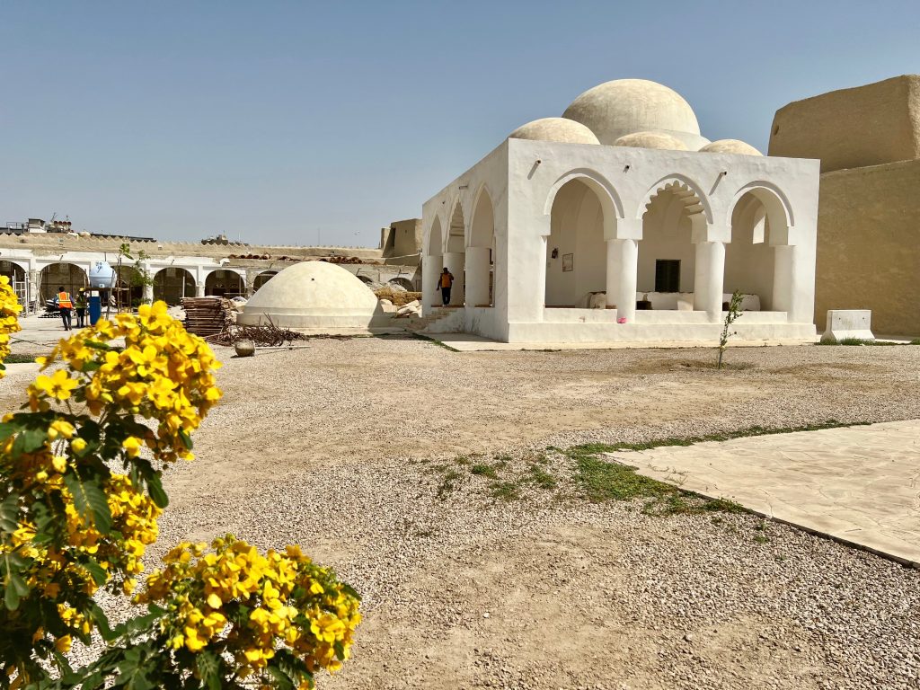 a white stone building with a domed roof and archways protecting an outside corridor