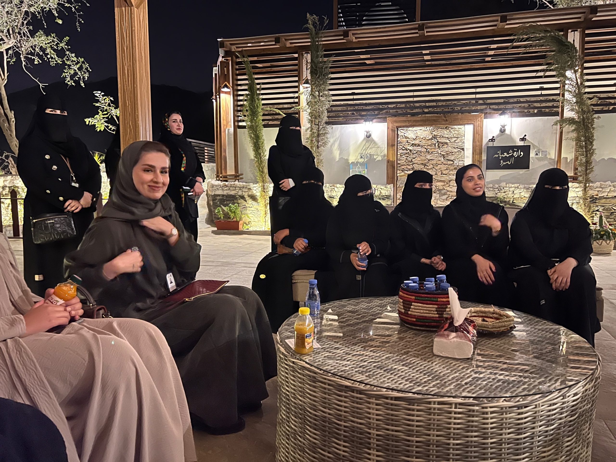 women in black abayas, some where a niqab, seated outdoors around a table