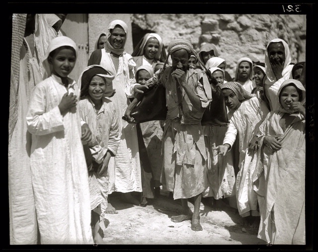 an Arab man with a large bag surrounded by children and adults