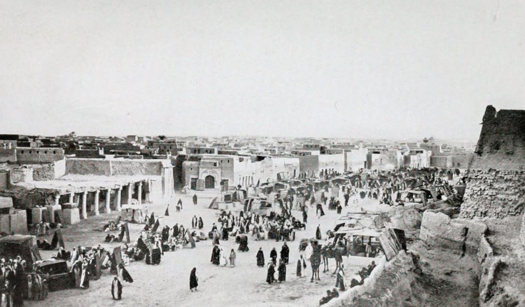 looking down on a busy market with men and women in Arabian Peninsula dress in a black and white photo