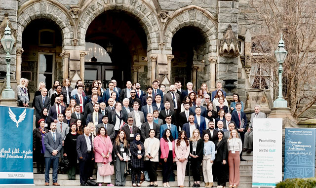 a group of approximately 40 people standing together on the stairs of an old stone building with large arches