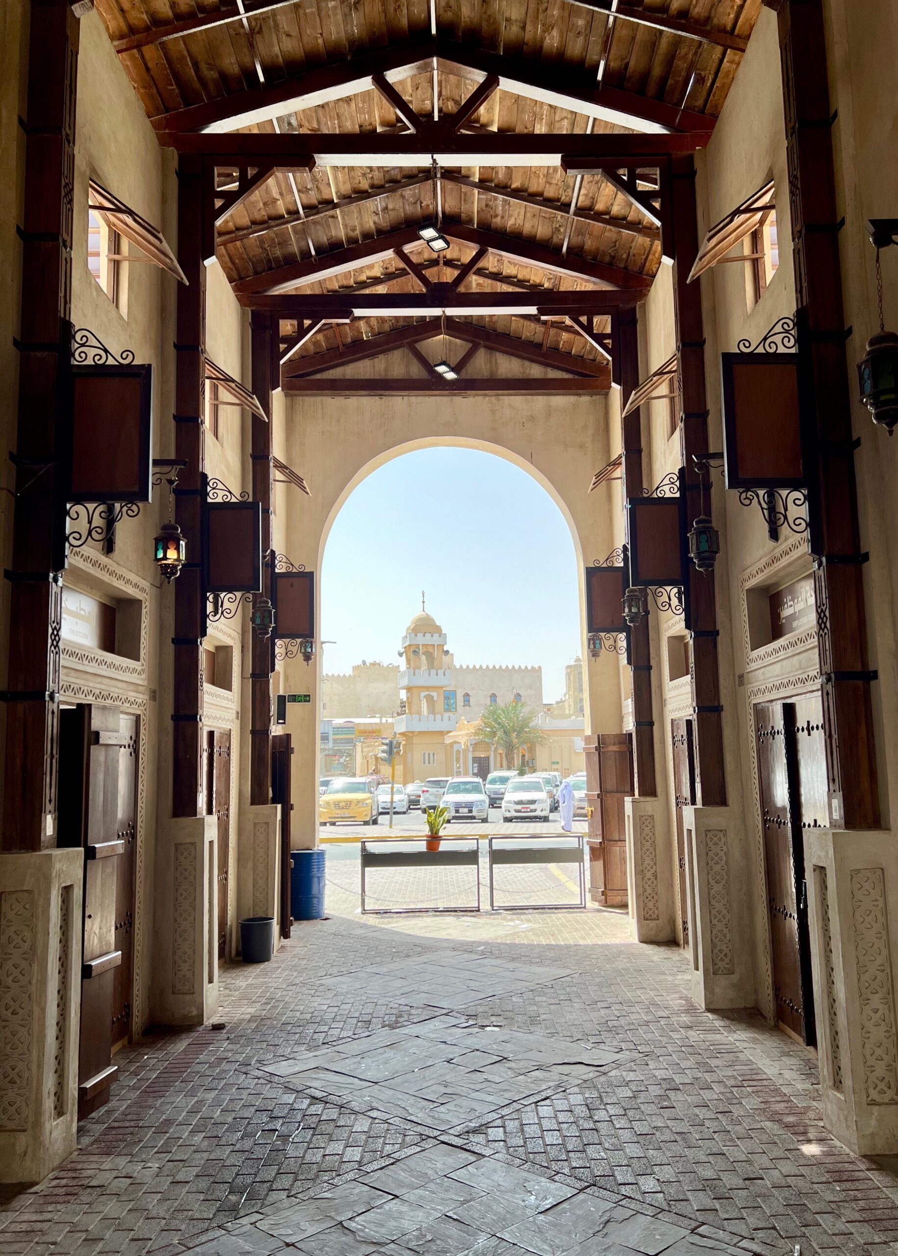 an archway at the end of a roofed corridor with buildings visible beyond the opening