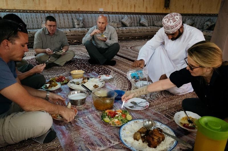 On our last day in Oman, an Omani family graciously hosted us for lunch in their home in the mountainous area of Jebel Akhdar. The family’s stand-alone building for entertaining was built to the side of the main house. Overlapping rugs, beautiful window treatment, a painted ceiling, and classic Arab seating adorn the room. Badar put down a sheet of plastic and placed the food on top. We were offered utensils, although Omanis usually eat with their hands. The food was fresh, traditional, and delicious. Here delegation members feast on chicken, rice, salad and, of course, lamb.